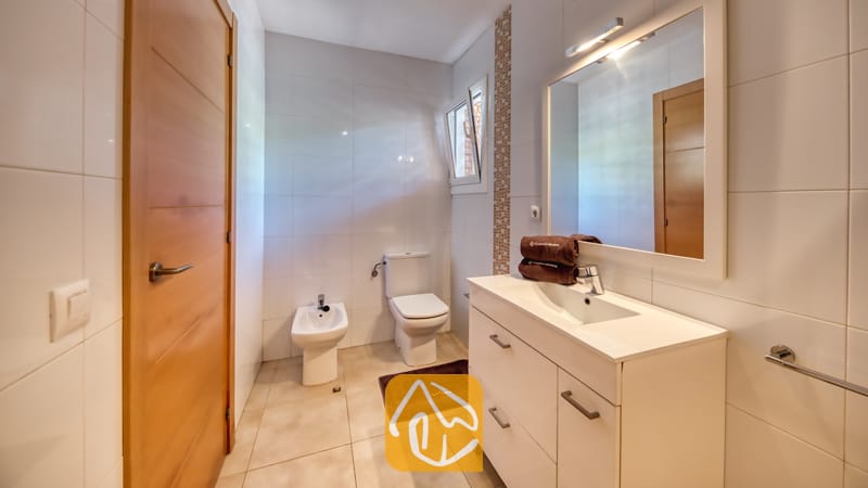 Vakantievilla's Costa Brava Spanje - Villa Lloret - Moderne badkamer met wit betegelde muren, een wit badmeubel met waskom en grote spiegel, een toilet en een bidet.