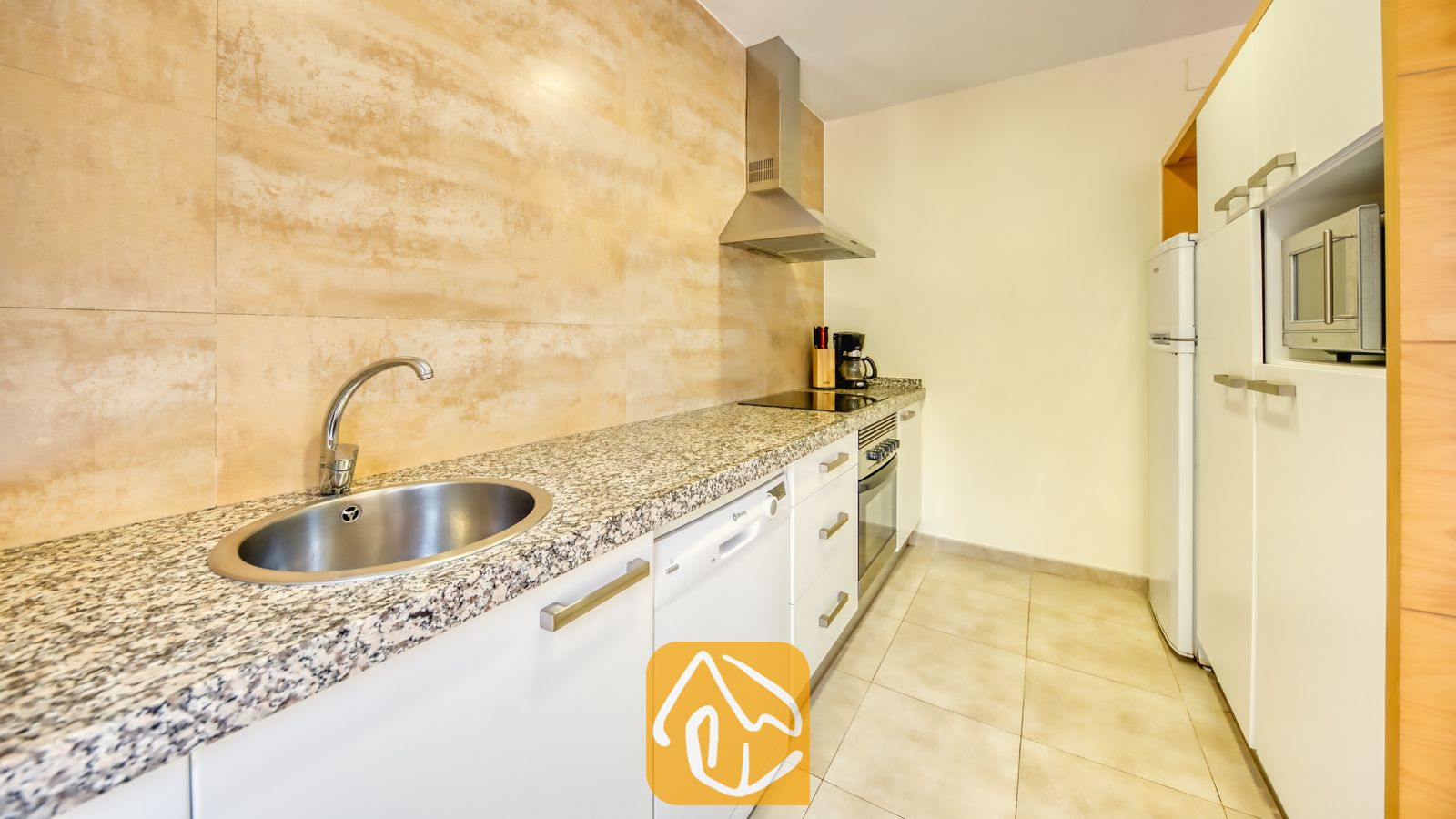 Vakantievilla's Costa Brava Spanje - Villa Lloret - Aanrecht met een ronde roestvrijstalen spoelbak, granieten werkbladen en witte kasten tegen een gestructureerde, beige tegelachterwand.