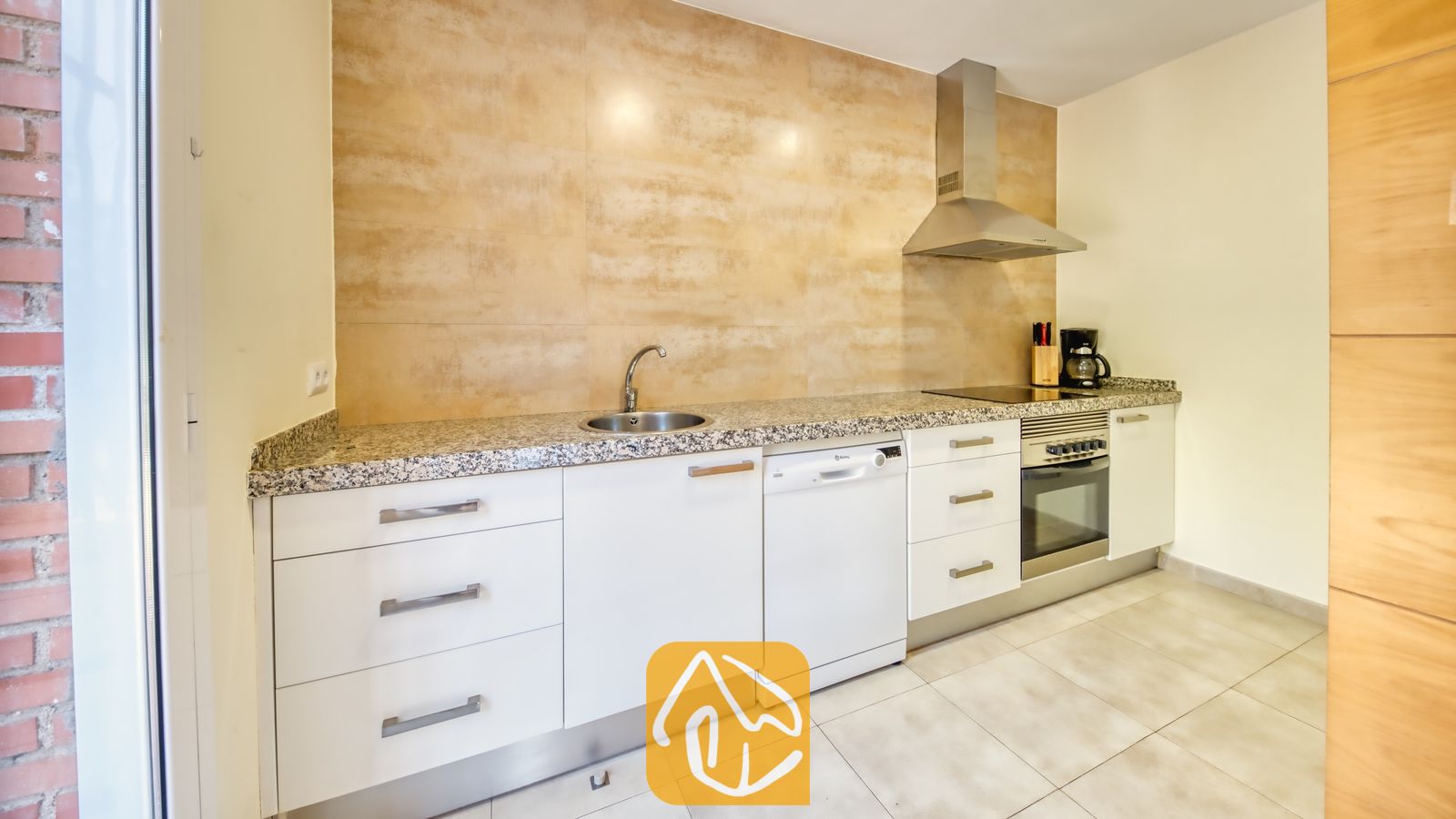 Vakantievilla's Costa Brava Spanje - Villa Lloret - Moderne keuken met witte kasten, gespikkelde granieten aanrechtbladen en getextureerde beige achterwandtegels.