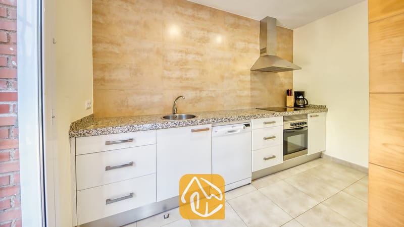 Vakantievilla's Costa Brava Spanje - Villa Lloret - Moderne keuken met witte kasten, gespikkelde granieten aanrechtbladen en getextureerde beige achterwandtegels.