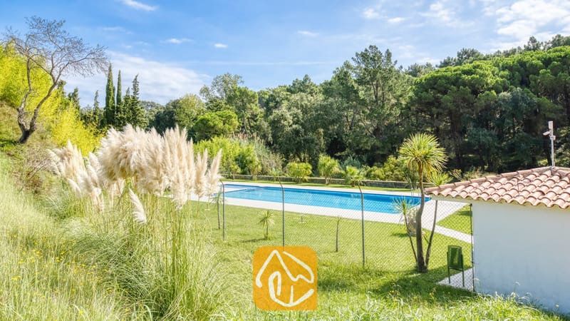 Vakantievilla's Costa Brava Spanje - Villa Lloret - Privé buitenzwembad bij Villa Lloret, omgeven door een gaashekwerk, hoog pampasgras, groene gazons en een dicht bos.