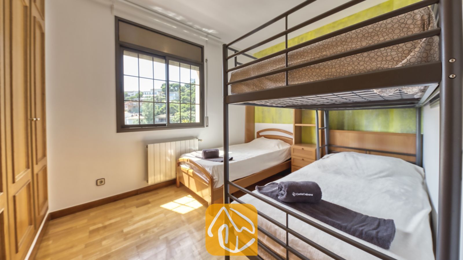 Vakantievilla's Costa Brava Spanje - Villa Paris - Slaapkamer met een donker metalen stapelbed, houten vloer, een eenpersoons houten bed en een raam met uitzicht op groen.