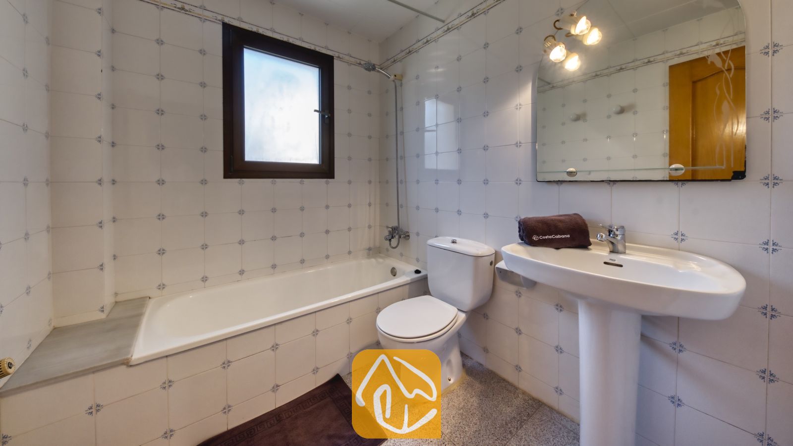 Vakantievilla's Costa Brava Spanje - Villa Paris - Badkamer met ligbad, witte kolomwastafel, toilet en blauw-gemeneerde tegelwanden onder een wandspiegel.