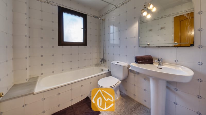 Villas de vacances Costa Brava Espagne - Villa Paris - Salle de bains équipée d'une baignoire, d'un lavabo blanc sur pied, de toilettes et de murs carrelés aux motifs bleus, surmontés d'un miroir mural.