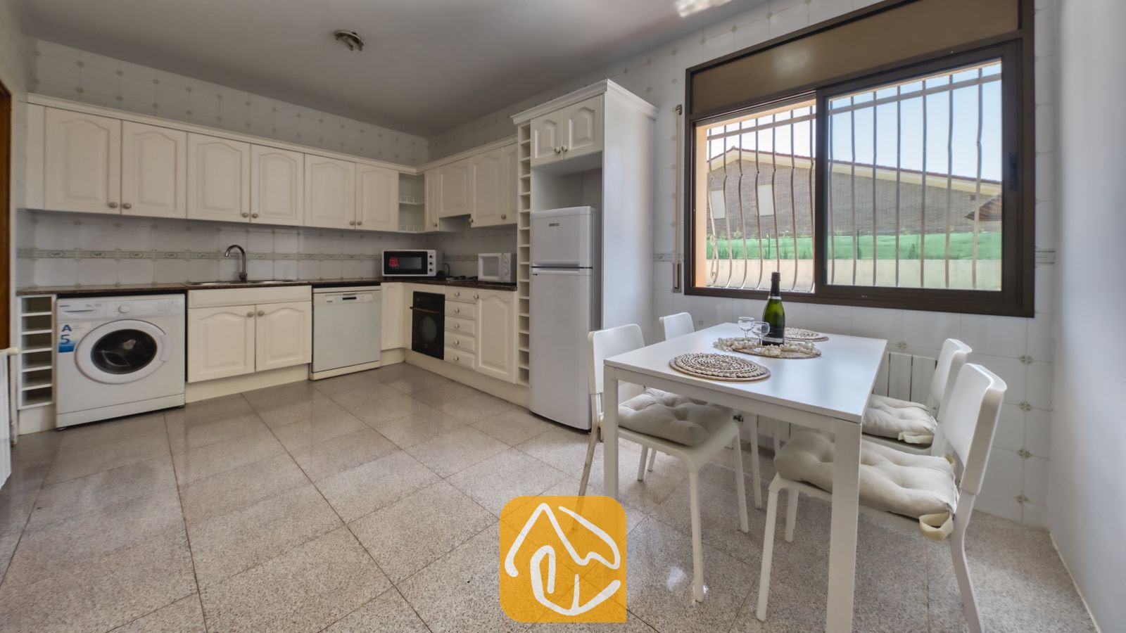Vakantievilla's Costa Brava Spanje - Villa Paris - Keuken met witte kasten, tegelvloer, een eettafel met vier stoelen en een raam met rolluiken.