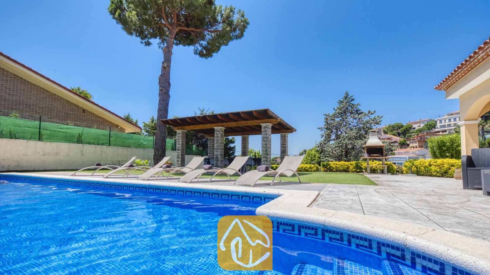 Vakantievilla's Costa Brava Spanje - Villa Paris - Privé-buitenzwembad bij Villa Paris met blauw getegelde randen, diverse ligstoelen op het terras, een overdekte pergola en een stenen barbecue op de achtergrond.