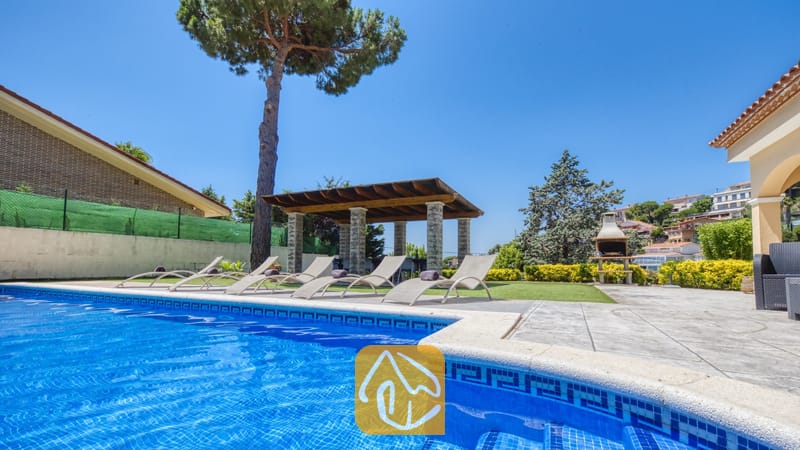 Vakantievilla's Costa Brava Spanje - Villa Paris - Privé-buitenzwembad bij Villa Paris met blauw getegelde randen, diverse ligstoelen op het terras, een overdekte pergola en een stenen barbecue op de achtergrond.