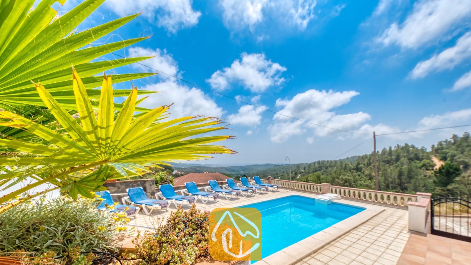 Vakantievilla's Costa Brava Spanje - Villa Santa Maria - Privézwembad met blauwe ligbedden en een tak van een palmprom op de voorgrond bij Villa Santa Maria onder een blauwe lucht met her en der wat wolken.