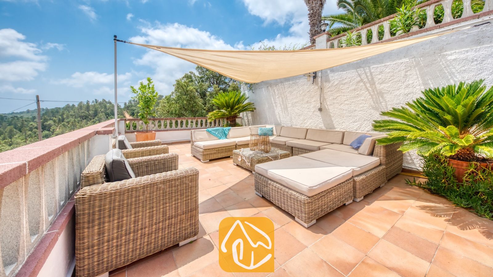Vakantievilla's Costa Brava Spanje - Villa Santa Maria - Terras van Villa Santa Maria met geweven rotan fauteuils, een grote hoekbank, beige kussens en een driehoekig schaduwdoek boven een tegelvloer.