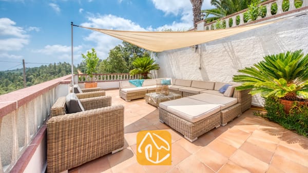 Vakantievilla's Costa Brava Spanje - Villa Santa Maria - Terras van Villa Santa Maria met geweven rotan fauteuils, een grote hoekbank, beige kussens en een driehoekig schaduwdoek boven een tegelvloer.