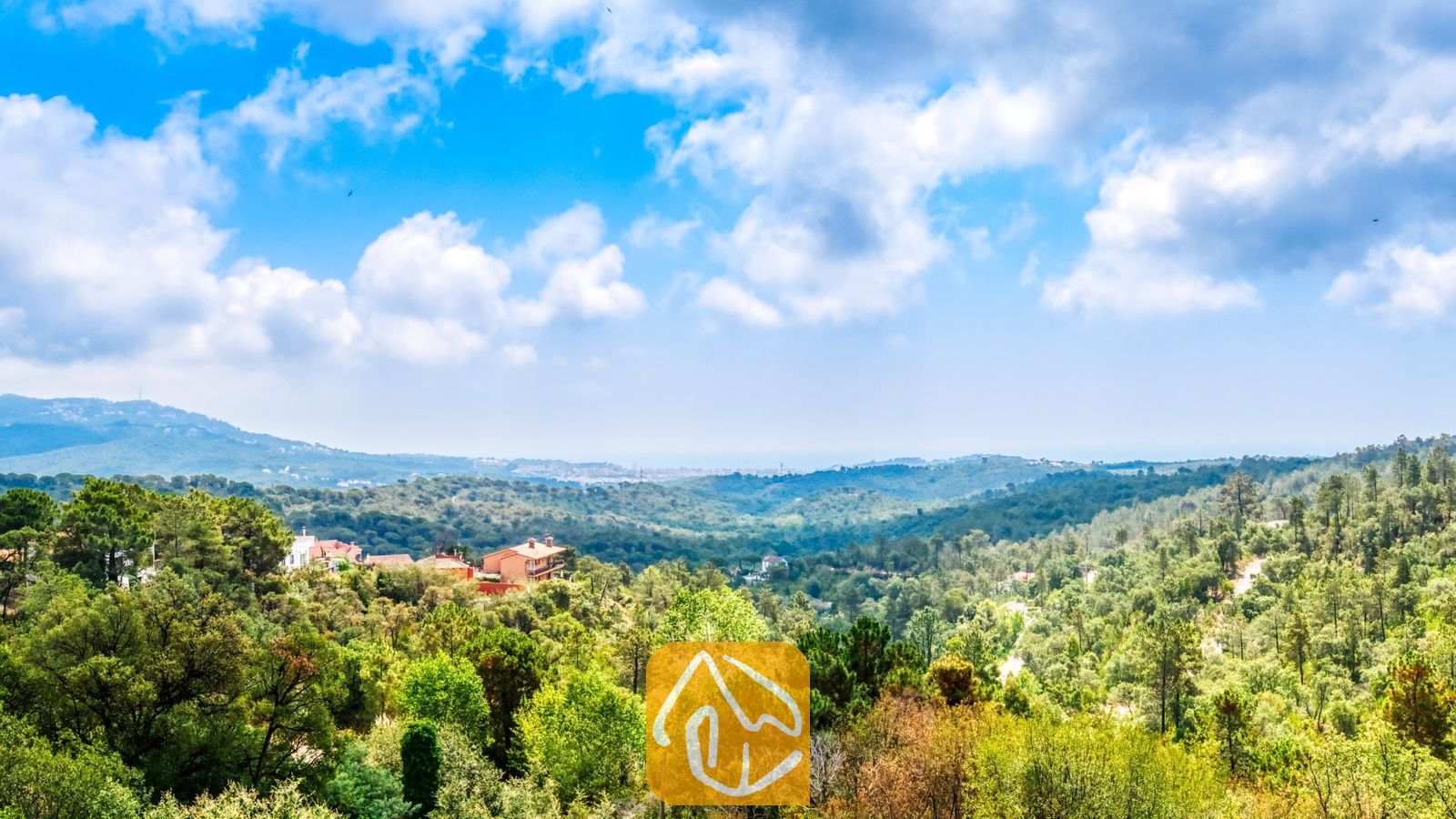 Vakantievilla's Costa Brava Spanje - Villa Santa Maria - Verheven uitzicht vanaf Villa Santa Maria met groene, bosrijke heuvels onder een blauwe lucht met witte wolken, en in de verte bebouwing aan de horizon.