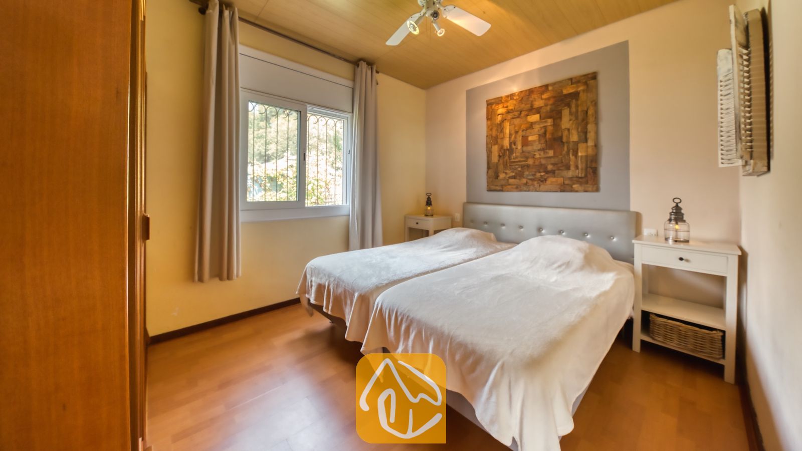 Vakantievilla's Costa Brava Spanje - Villa Santa Maria - Slaapkamer met twee eenpersoonsbedden, wittelinnen beddengoed, houten vloeren en een groot, abstract houten wandkunstwerk boven het grijze hoofdeinde.
