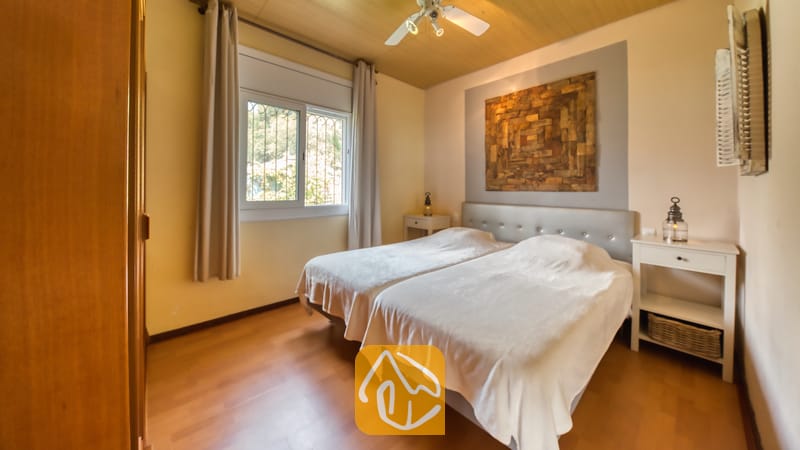Villas de vacances Costa Brava Espagne - Villa Santa Maria - Chambre avec deux lits simples, du linge de lit blanc, un parquet en bois et une grande œuvre d'art murale en bois abstrait au-dessus de la tête de lit grise.