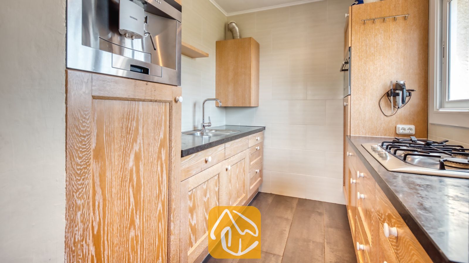 Vakantievilla's Costa Brava Spanje - Villa Santa Maria - Interieur van de keuken met lichte houten kasten, een donker aanrechtblad, een inbouw-koffiezetapparaat en een gaskookplaat.