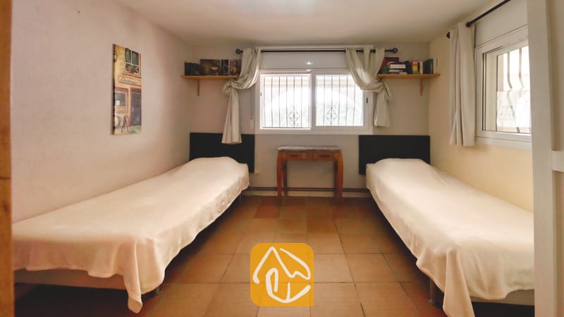 Villas de vacances Costa Brava Espagne - Villa Santa Maria - Chambre avec deux lits simples, sols carrelés, rideaux blancs et étagères murales.