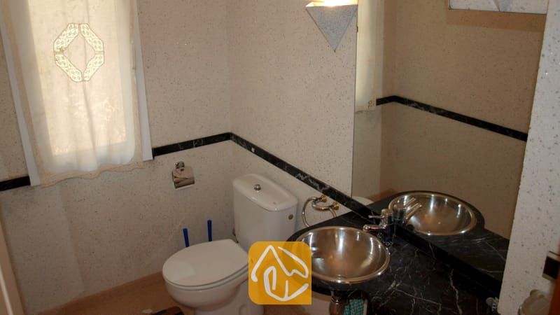 Villas de vacances Costa Brava Espagne - Villa Valentina - Salle de bains compacte comprenant des toilettes blanches, un plan de travail en marbre noir avec une vasque ronde en métal, ainsi qu'une fenêtre dépolie habillée d'un rideau à motifs.