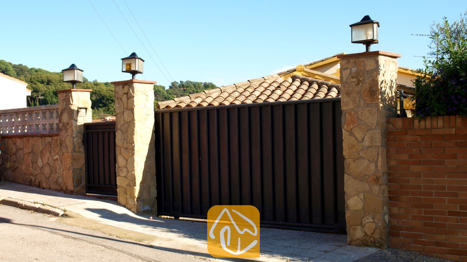 Vakantievilla's Costa Brava Spanje - Villa Valentina - Donkere metalen opritpoort omlijst door stenen pilaren met buitenlampen bij de ingang van Villa Valentina in Spanje