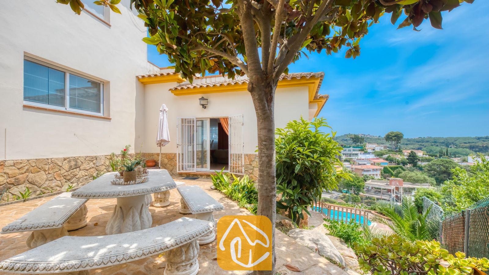 Vakantievilla's Costa Brava Spanje - Villa Valentina - Stenen terras bij Villa Valentina met een gehouwen stenen eettafel en banken, beschaduwd door een boom en met uitzicht op een schitterend landschap.