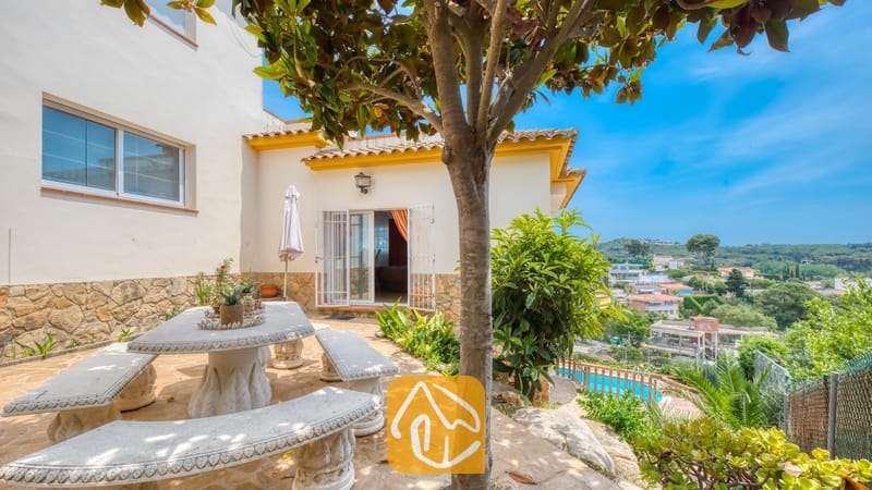 Vakantievilla's Costa Brava Spanje - Villa Valentina - Stenen terras bij Villa Valentina met een gehouwen stenen eettafel en banken, beschaduwd door een boom en met uitzicht op een schitterend landschap.