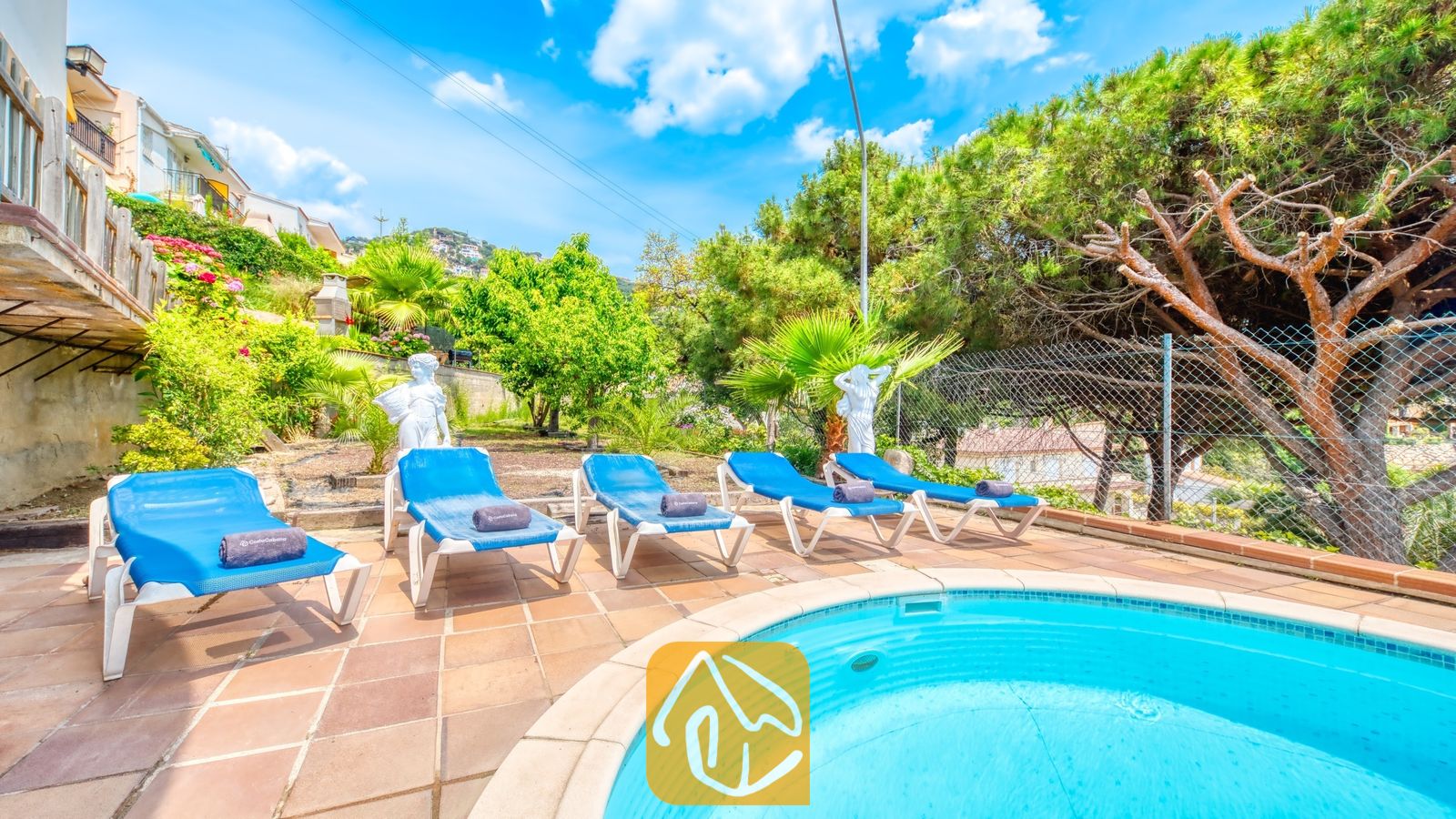 Vakantievilla's Costa Brava Spanje - Villa Valentina - Rond zwembad bij Villa Valentina, omringd door blauwe ligbedden, terracotta tegels en groene bomen onder een helderblauwe hemel.