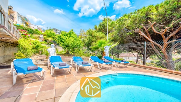 Vakantievilla's Costa Brava Spanje - Villa Valentina - Rond zwembad bij Villa Valentina, omringd door blauwe ligbedden, terracotta tegels en groene bomen onder een helderblauwe hemel.