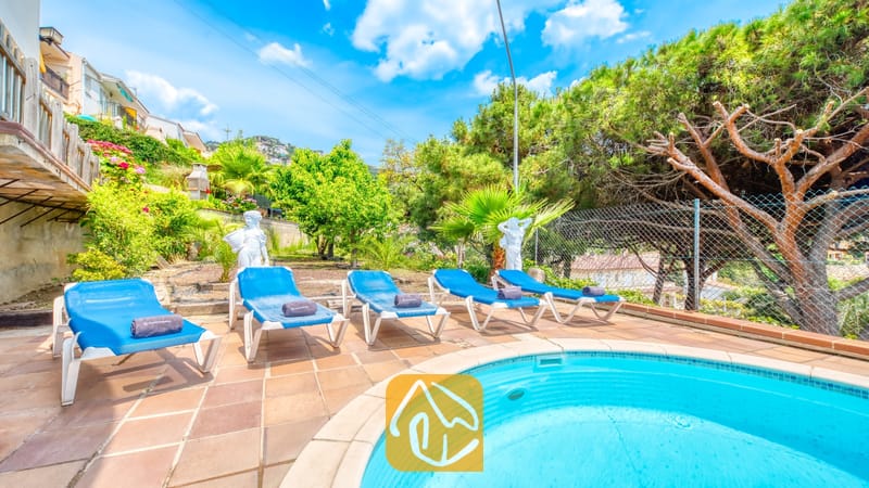 Vakantievilla's Costa Brava Spanje - Villa Valentina - Rond zwembad bij Villa Valentina, omringd door blauwe ligbedden, terracotta tegels en groene bomen onder een helderblauwe hemel.