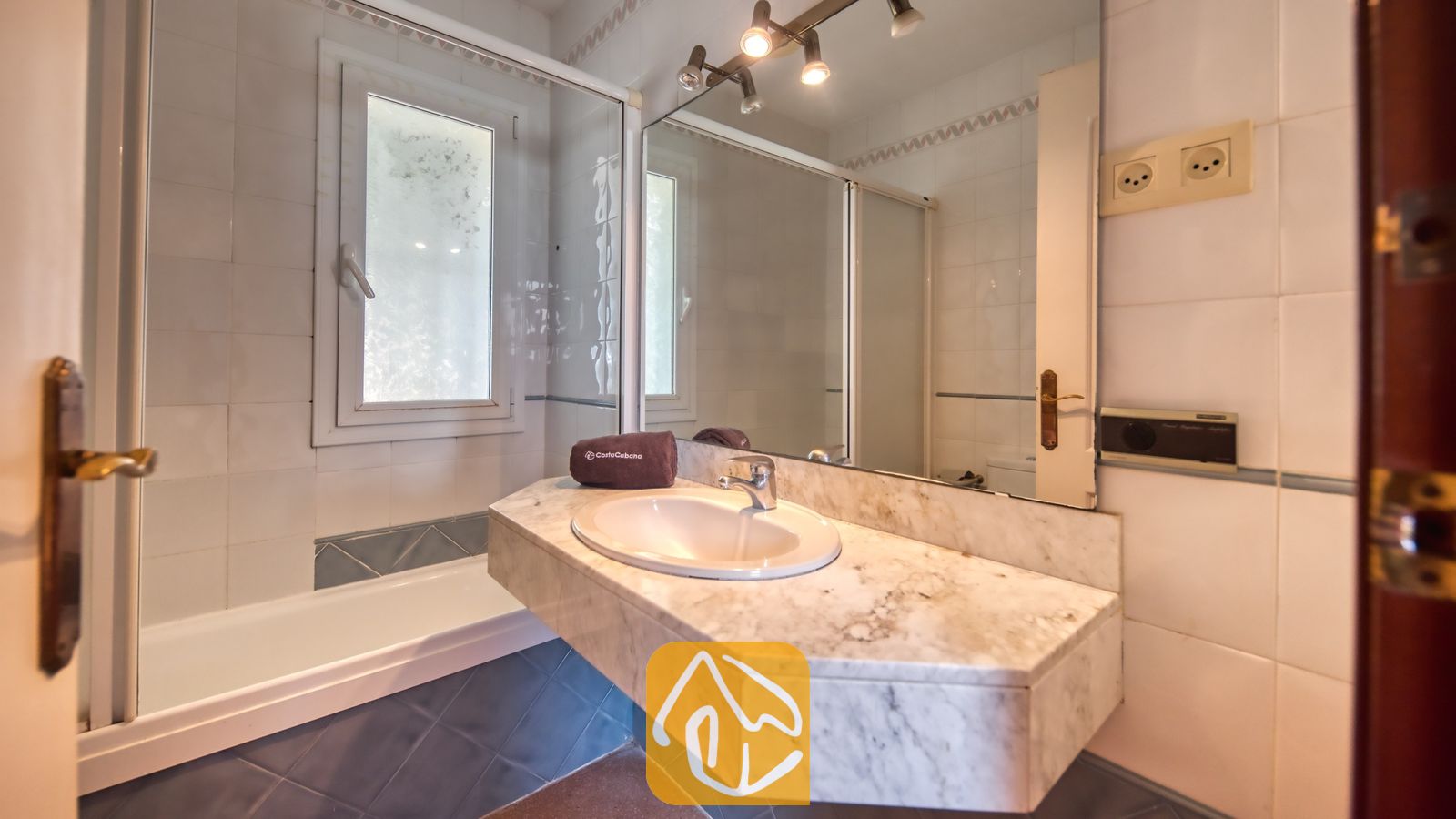 Vakantievilla's Costa Brava Spanje - Villa Valentina - Badkamer voorzien van een wastafelmeubel met marmeren blad en een grote wandspiegel, een ligbad met glazen wand en witte wandtegels.