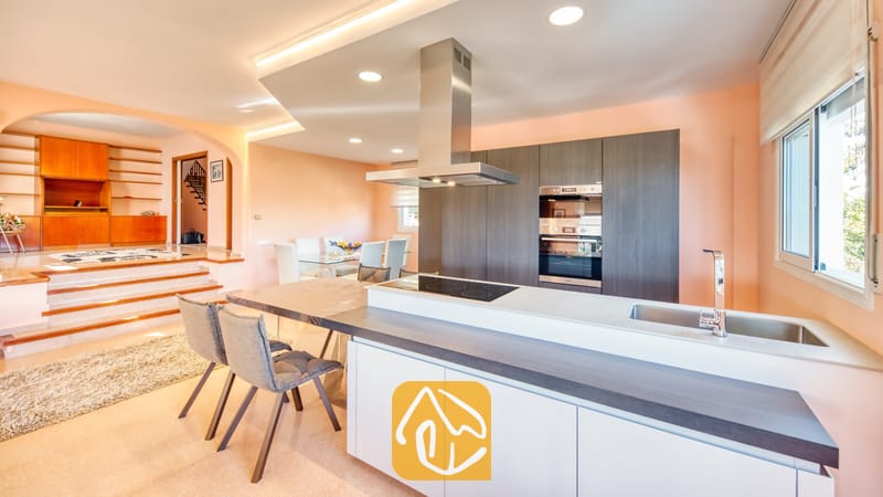 Vakantievilla's Costa Brava Spanje - Villa Valentina - Moderne keuken met donkere houten kasten, een roestvrijstalen afzuigkap en een aangrenzende eethoek met een trap naar een verhoogde woonkamer.