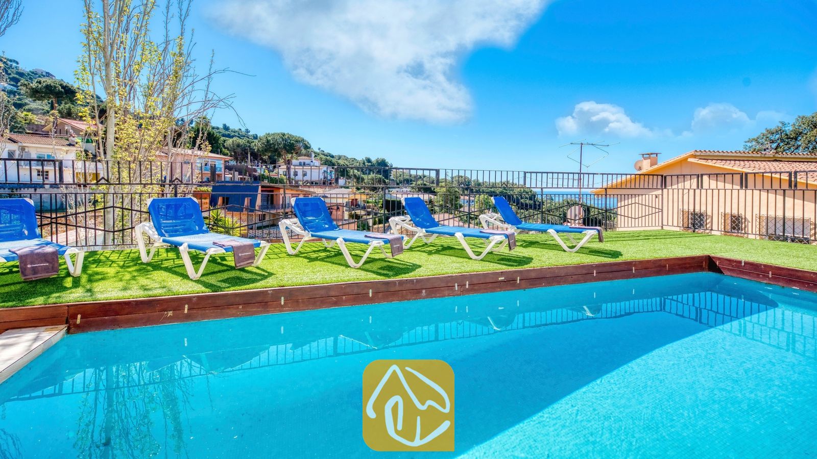 Vakantievilla's Costa Brava Spanje - Villa Donna - Buitenzwembad met helderblauw water bij Villa Donna, voorzien van vier wit-blauwe ligstoelen op kunstgras onder een heldere hemel.