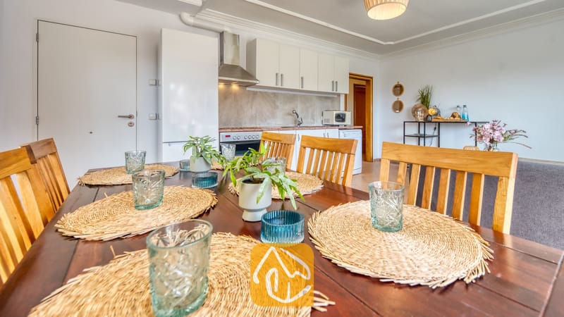 Vakantievilla's Costa Brava Spanje - Villa Donna - Houten eettafelset met geweven placemats en glaswerk, met een open keuken op de achtergrond.