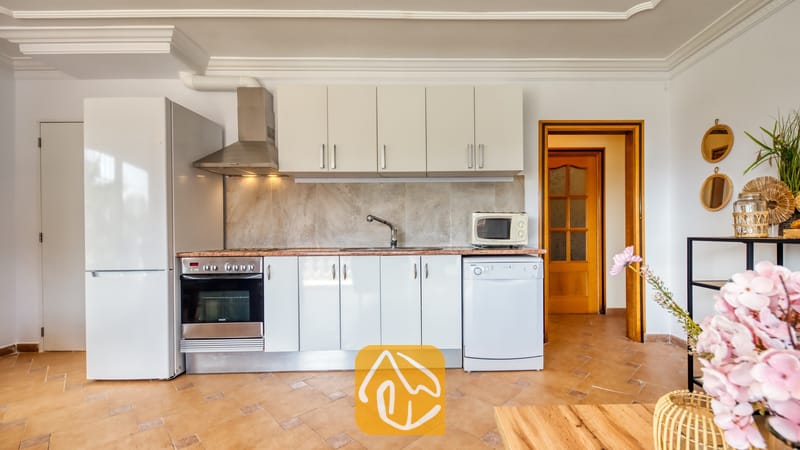 Vakantievilla's Costa Brava Spanje - Villa Donna - Keukeninterieur met witte kasten, roestvrijstalen apparatuur, een betegelde achterwand en bruine plavuizen.
