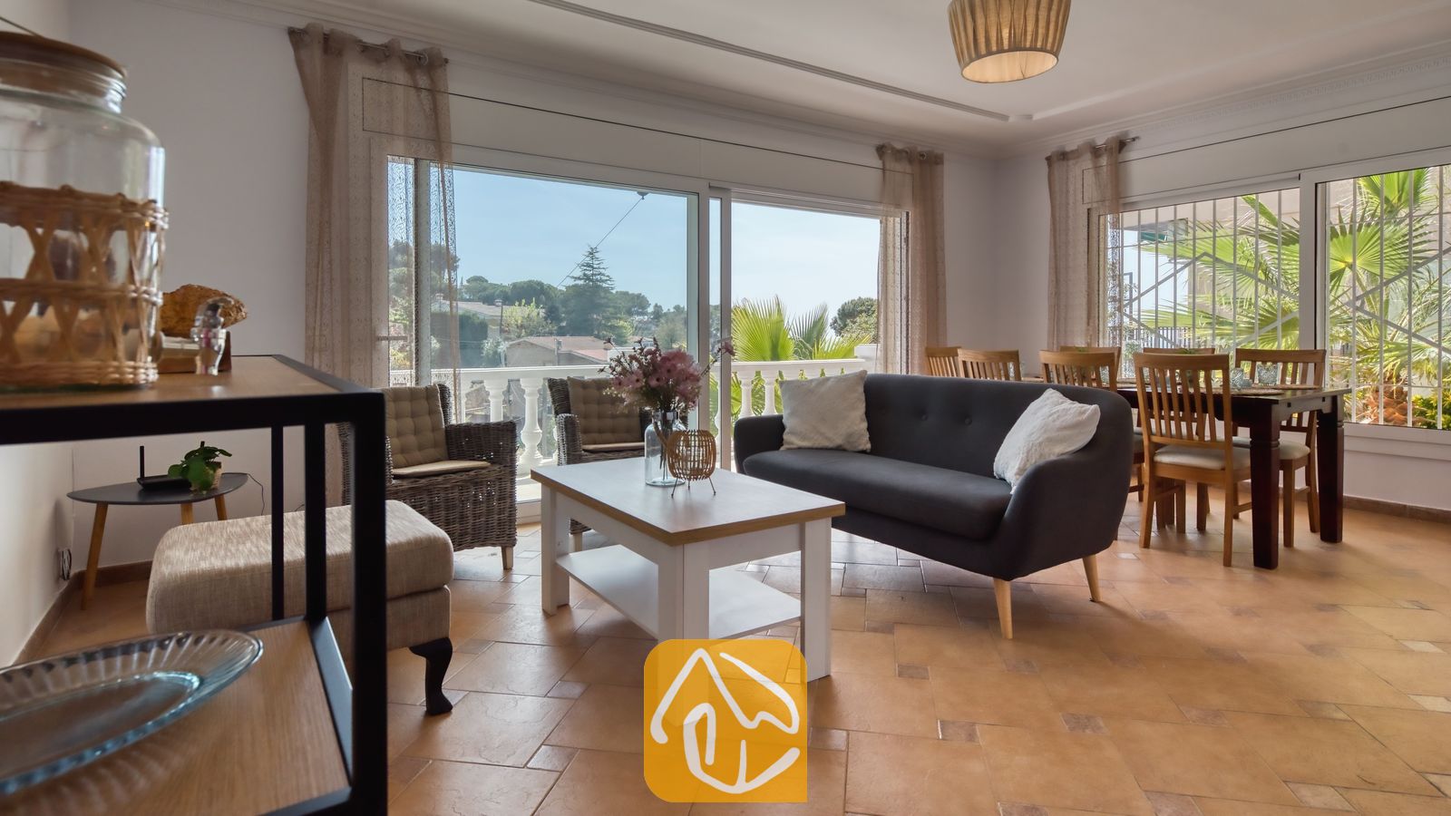 Vakantievilla's Costa Brava Spanje - Villa Donna - Woonkamer van Villa Donna met een donkergrijze bank, een witte salontafel en grote glazen schuifdeuren die opengaan naar een balkon met uitzicht naar buiten.