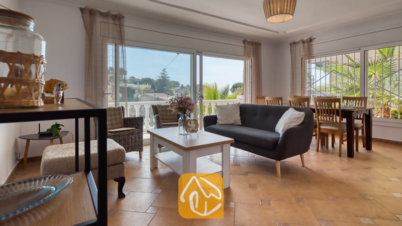 Vakantievilla's Costa Brava Spanje - Villa Donna - Woonkamer van Villa Donna met een donkergrijze bank, een witte salontafel en grote glazen schuifdeuren die opengaan naar een balkon met uitzicht naar buiten.