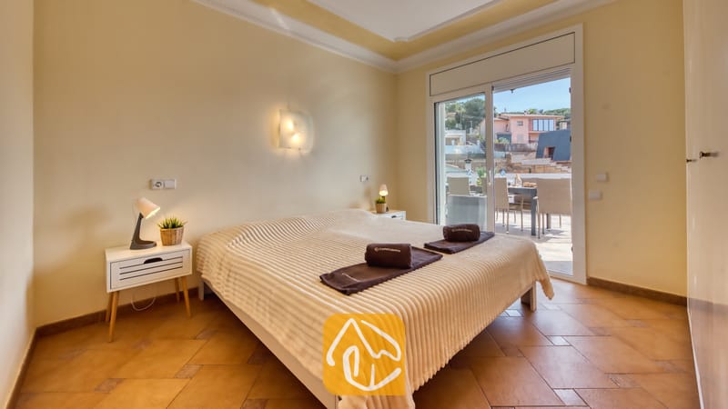 Vakantievilla's Costa Brava Spanje - Villa Donna - Slaapkamer in Villa Donna met een tweepersoonssbed, een witte geweven sprei, opgerolde donkere handdoeken en glazen schuifdeuren die opengaan naar een buitenterras
