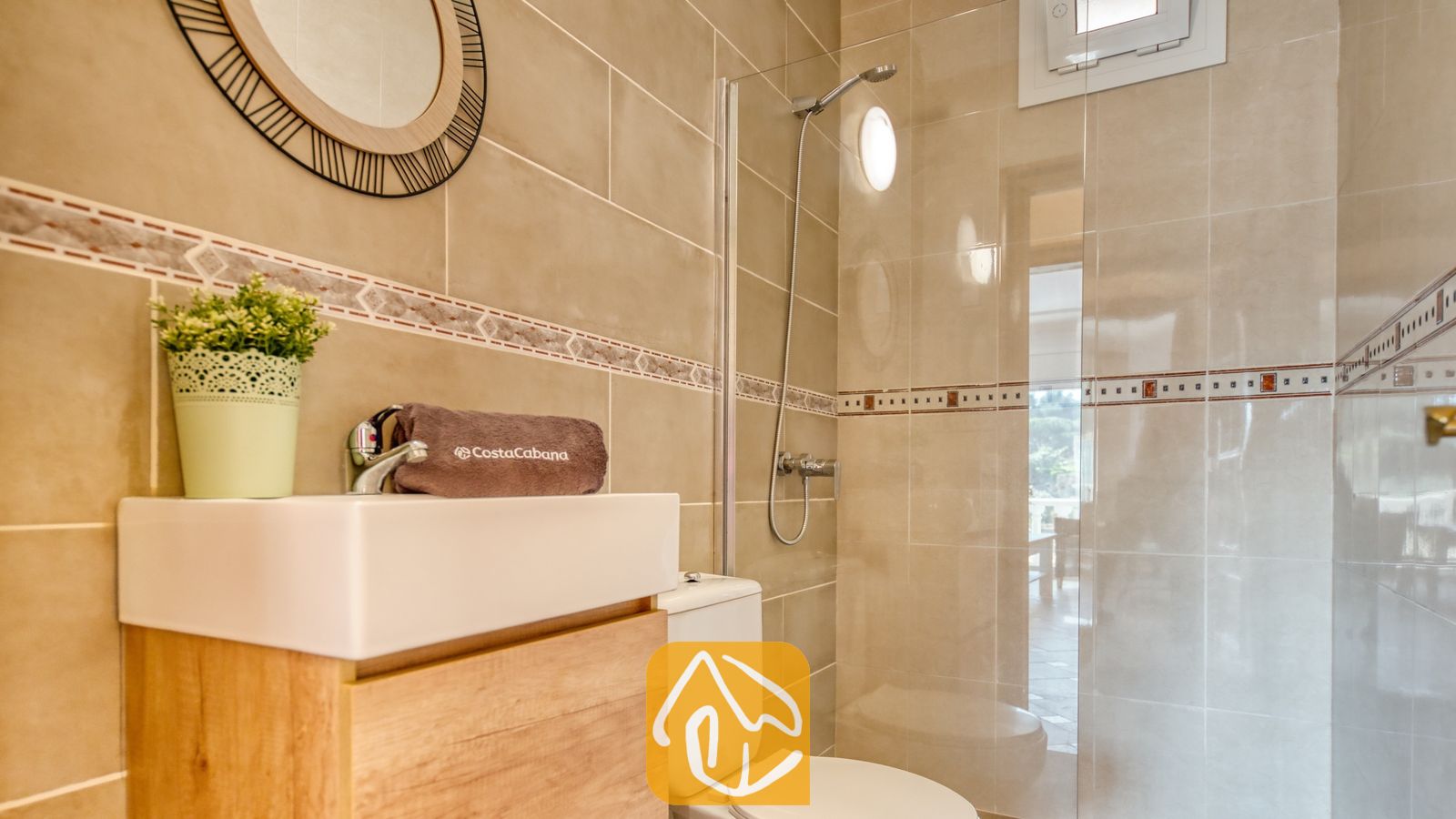 Vakantievilla's Costa Brava Spanje - Villa Donna - Moderne badkamer met betegelde muren in een beigetint, een houtenwastafelmeubel met een witte waskom, een ronde decoratieve spiegel en een glazen inloopdouche.