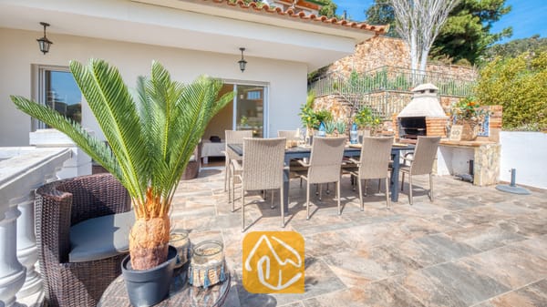 Vakantievilla's Costa Brava Spanje - Villa Donna - Zonnig terras bij Villa Donna, voorzien van een eettafel voor buiten met rieten stoelen, een ingebouwde stenen barbecue en betegelde vloeren.