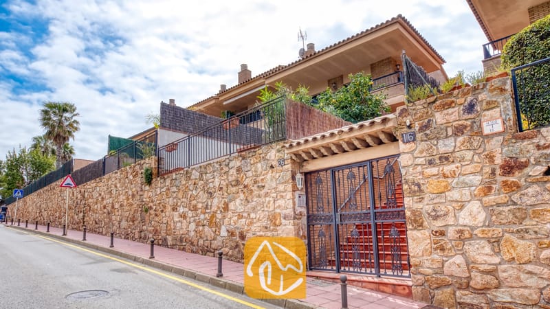 Holiday villas Costa Brava Spain - Casa Costa - Exterior view of Casa Costa showing a stone retaining wall, dark metal gate, and multi-level building facade with balconies.