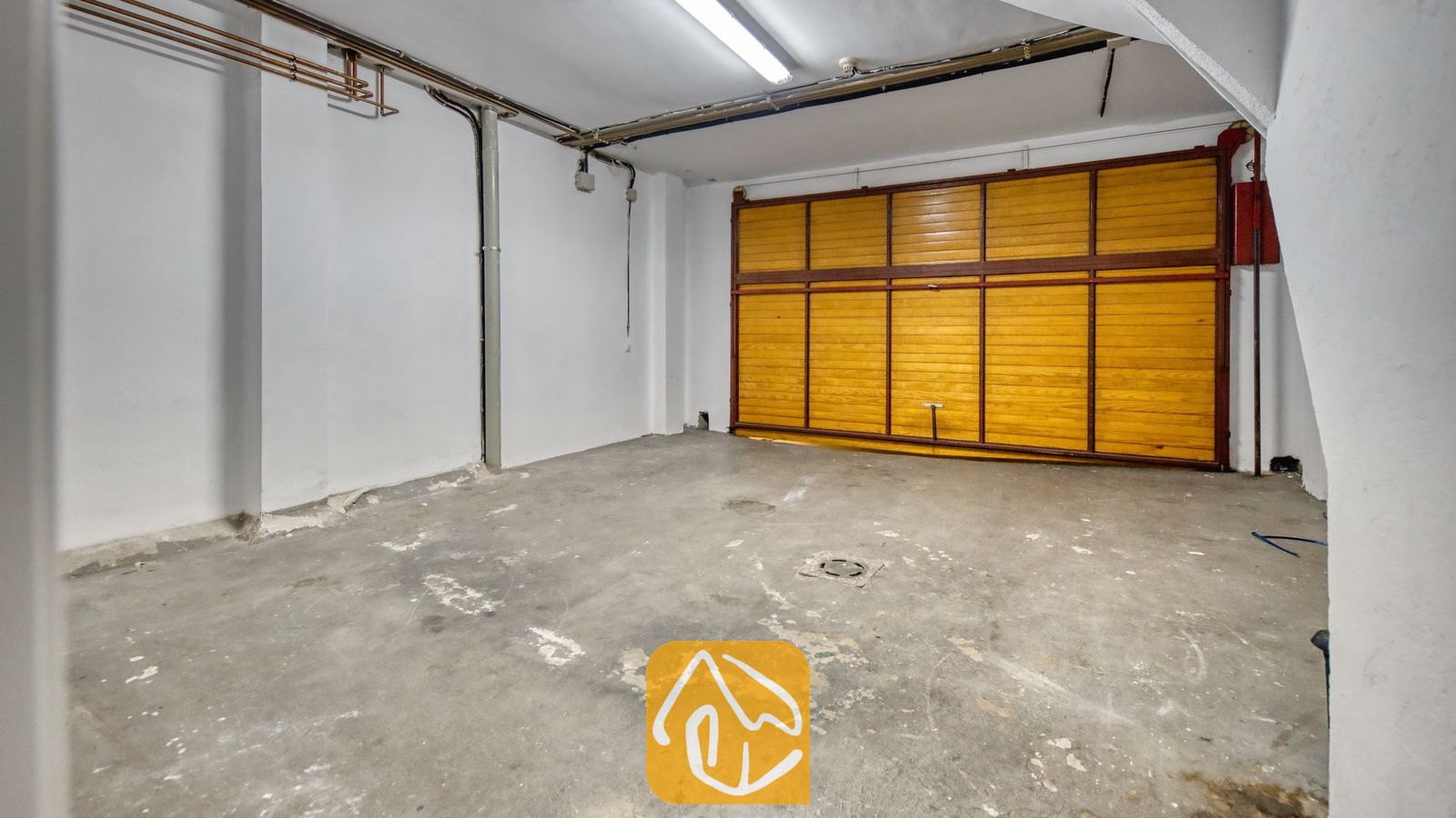 Vakantievilla's Costa Brava Spanje - Casa Costa - Binnenparkeerplaats bij Casa Costa met witte muren, een betonnen vloer en een grote houten paneeldeur.