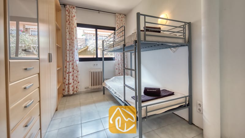 Holiday villas Costa Brava Spain - Casa Costa - Bedroom furnished with a gray metal bunk bed, light wood wardrobe with drawers, and floral curtains framing the window.