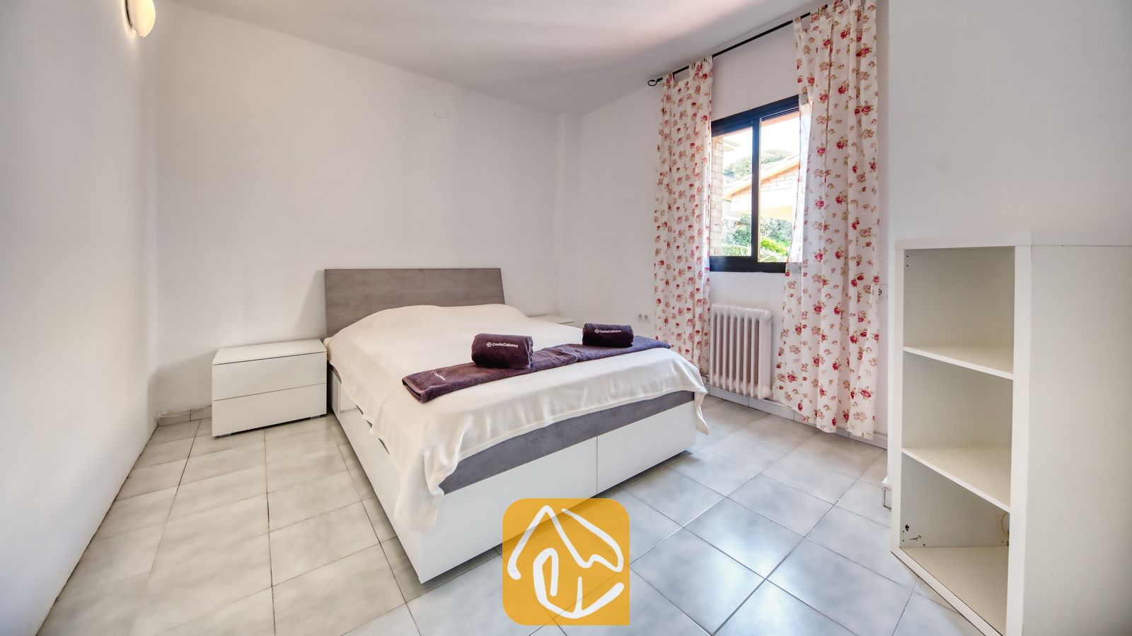 Vakantievilla's Costa Brava Spanje - Casa Costa - Slaapkamer met een tweepersoonsbed, witte tegelvloeren, bloemetjesgordijnen en een nachtkastje bij Casa Costa