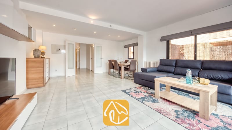 Vakantievilla's Costa Brava Spanje - Casa Costa - Ruime woon- en eetkamer bij Casa Costa met een donkerblauwe hoekbank, een lichte houten salontafel en een bloemetjestapijt op een tegelvloer.