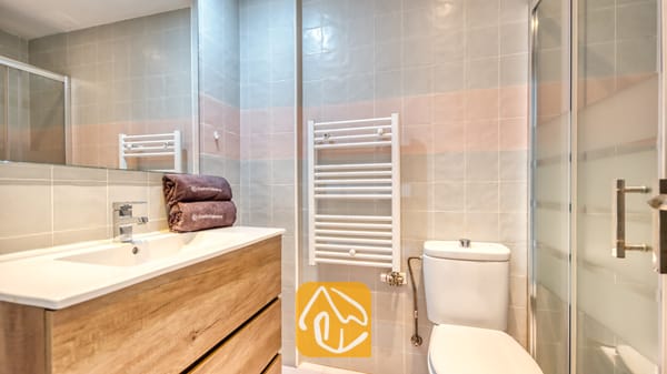 Vakantievilla's Costa Brava Spanje - Casa Costa - Moderne badkamer met een houten badkamermeubel en een witte wastafel, een wandgemonteerd wit handdoekenrek en betegelde muren in grijze en roze tinten.