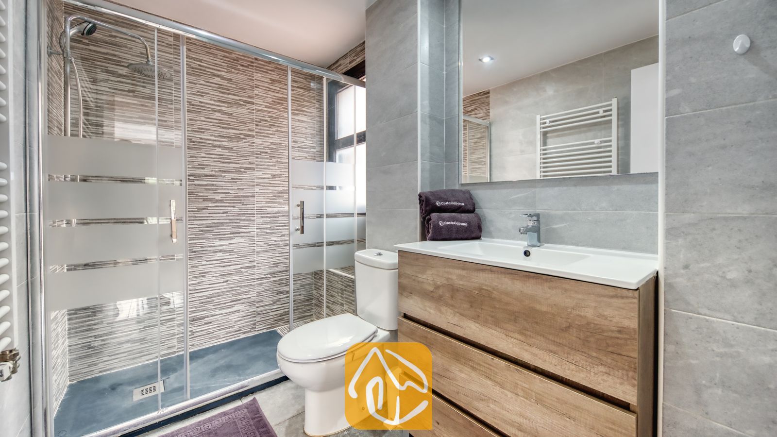 Vakantievilla's Costa Brava Spanje - Casa Costa - Moderne badkamer met een inloopregendouche met glazen wand, houten badkamermeubel met een witte wastafel en grijs getegelde muren.