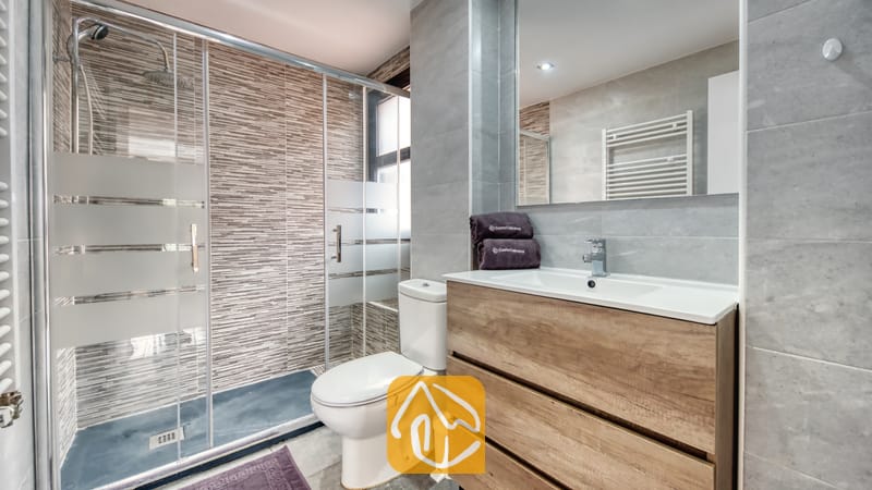 Holiday villas Costa Brava Spain - Casa Costa - Modern bathroom with a walk-in glass shower, wooden vanity with a white basin, and gray tile walls.
