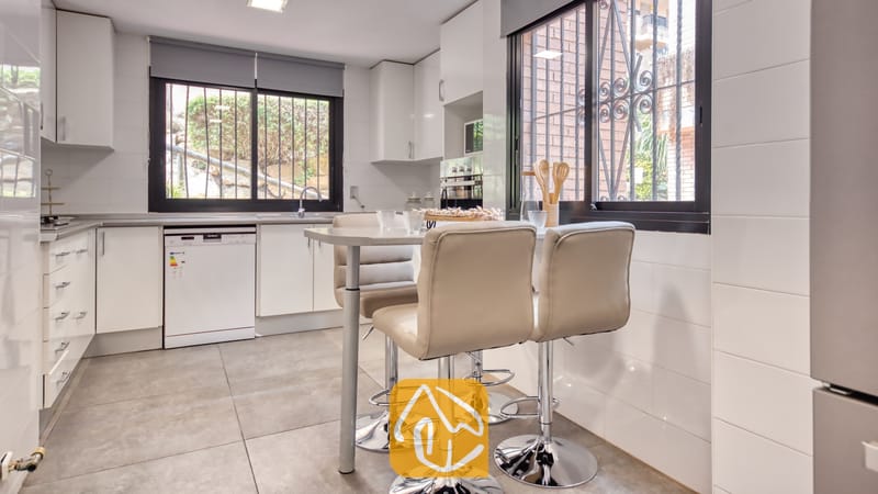 Vakantievilla's Costa Brava Spanje - Casa Costa - Moderne keuken met witte kasten, een kleine eettafel en drie lichtbeige barstoelen tegen een achtergrond van grijs tegelwerk.