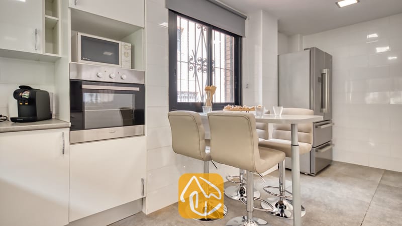 Vakantievilla's Costa Brava Spanje - Casa Costa - Moderne keuken met witte betegelde muren, een inbouw oven van roestvrij staal, een magnetron en een hoge eettafel met vier beige barstoelen.