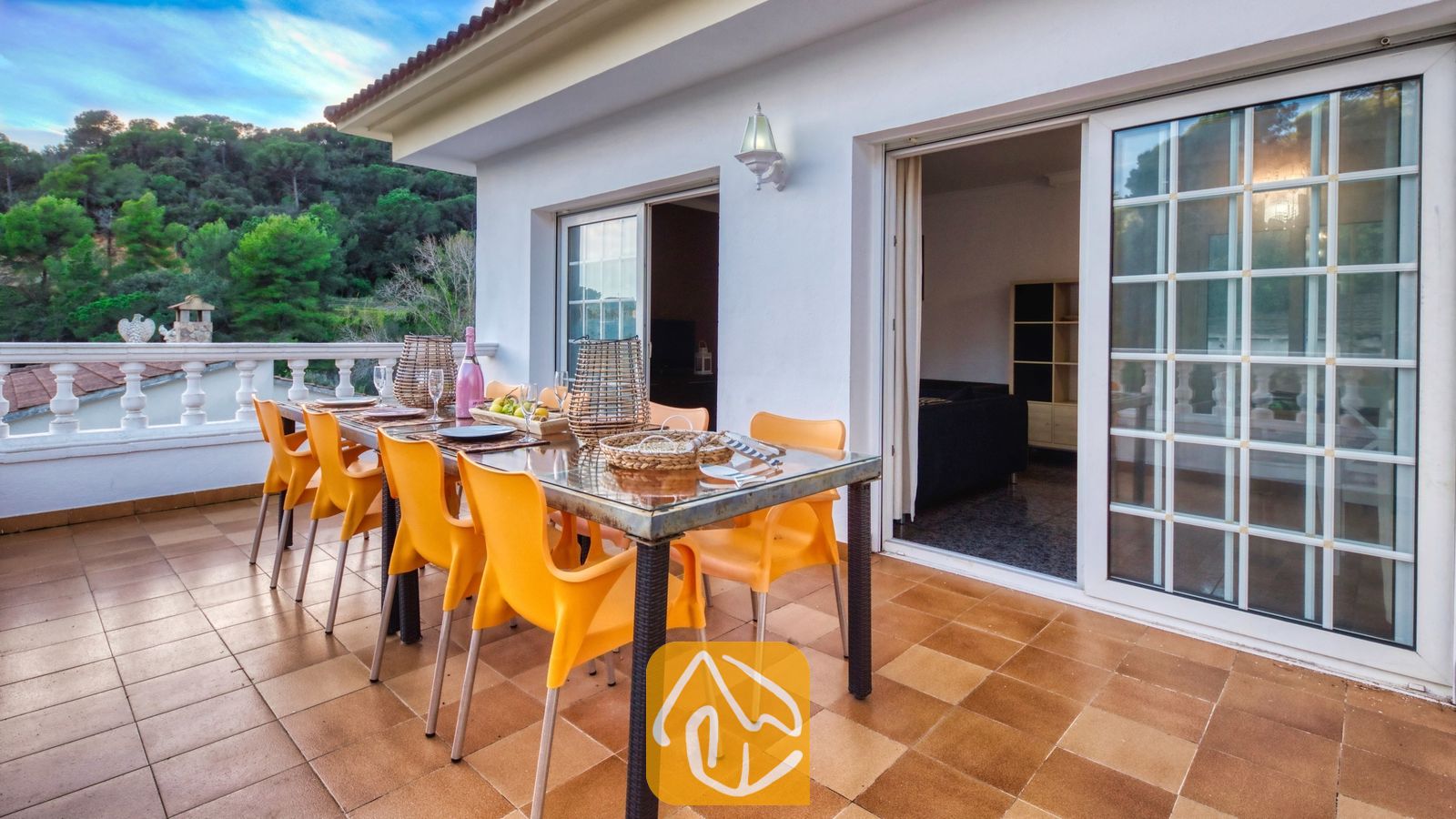 Vakantievilla's Costa Brava Spanje - Villa Rosa - Terras bij Villa Rosa met een glazen eettafel, felle oranje stoelen en glazen schuifdeuren die uitkomen op het interieur.
