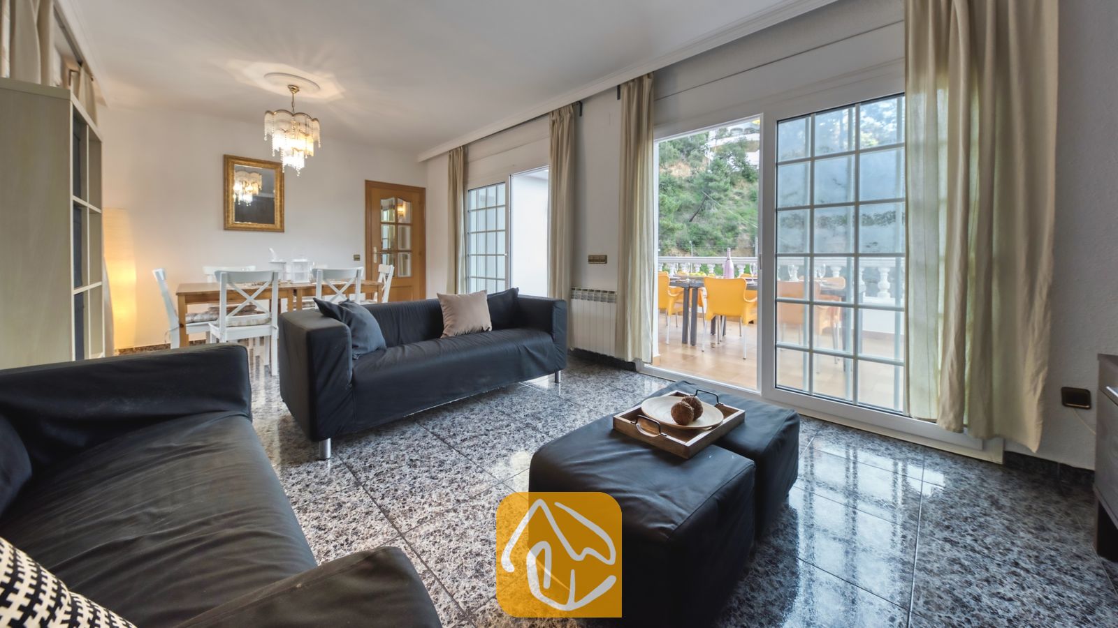 Vakantievilla's Costa Brava Spanje - Villa Rosa - Ruime woonkamer in Villa Rosa met donkergrijze banken, gepolijste stenen tegelvloeren en grote glazen schuifdeuren die uitkomen op een buitenterras.