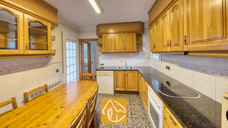 Vakantievilla's Costa Brava Spanje - Villa Rosa - Keuken voorzien van houten kasten, donkere granieten aanrechtbladen en een geïntegreerde eettafel met bijpassende houten stoelen.