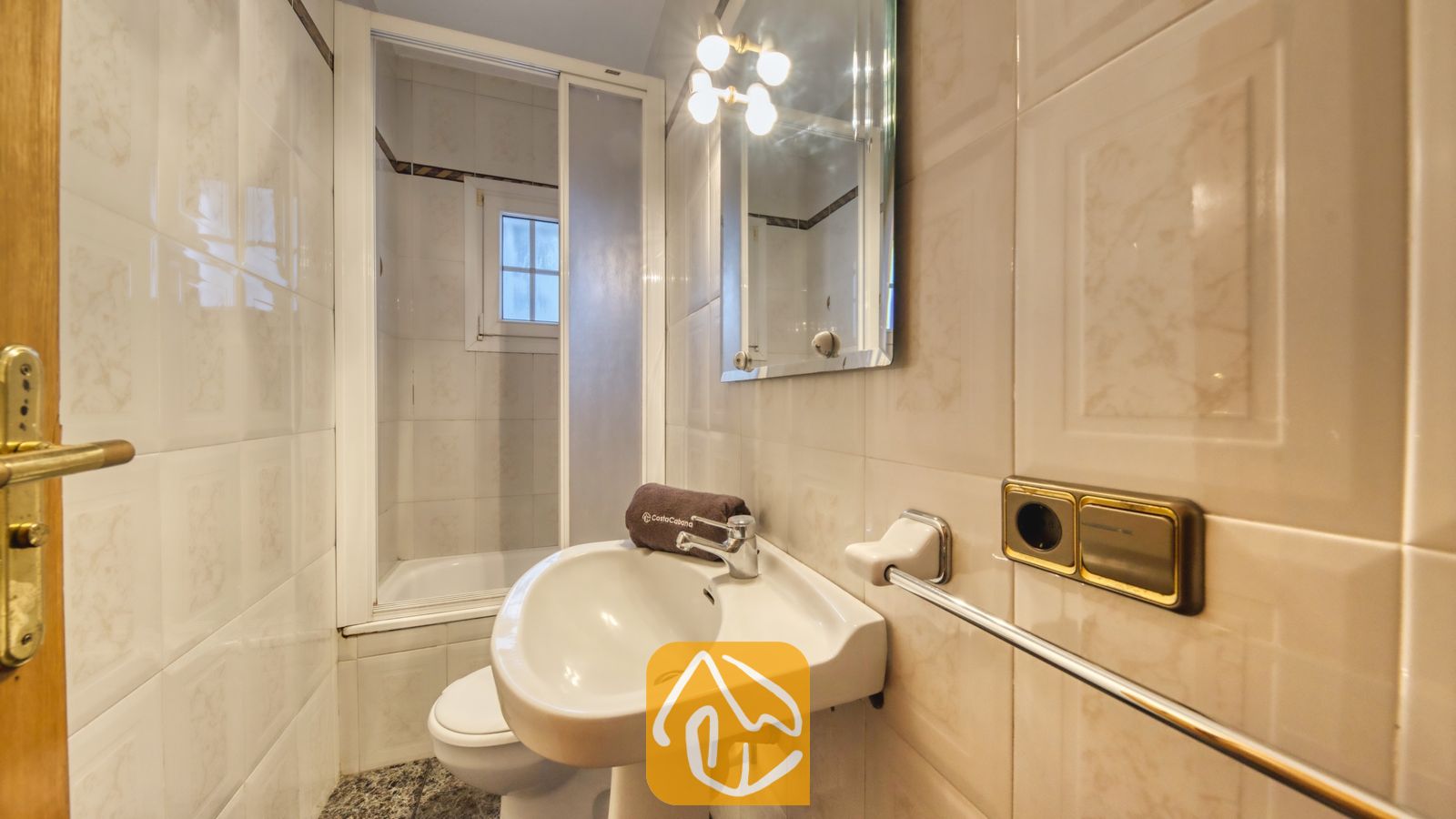 Vakantievilla's Costa Brava Spanje - Villa Rosa - Badkamer met een witte vrijstaande wastafel met chromen kraan, een wandspiegel met armatuur met meerdere lichtbronnen en betegelde muren.